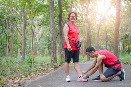 快乐的亚洲母亲和儿子在公园系鞋带老年人护理跑步者准备慢跑概念
