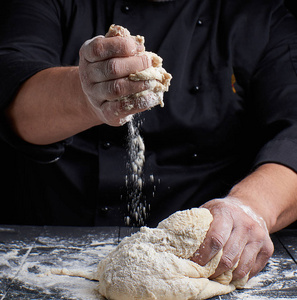 s hands knead white wheat flour yeast dough on a black wooden ta