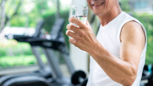 老年人运动后在健身房健身中心喝矿泉水。 老年人健康的生活方式。
