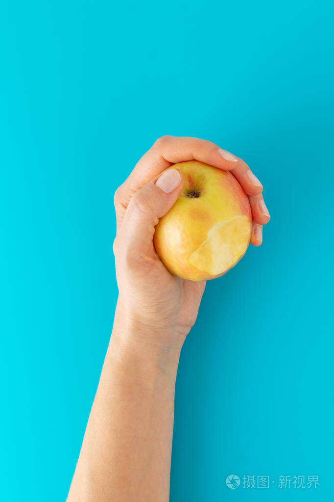 手拿着一个苹果在蓝色的背景上咬了一口