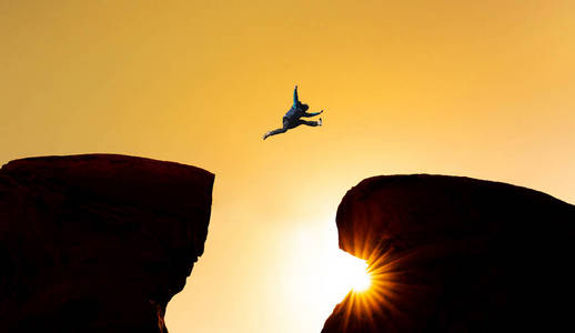 挑战风险和自由概念. 剪影一个人跳过悬崖照片