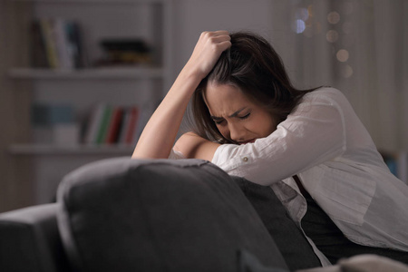 悲伤的女人抱怨晚上坐在家里的沙发上