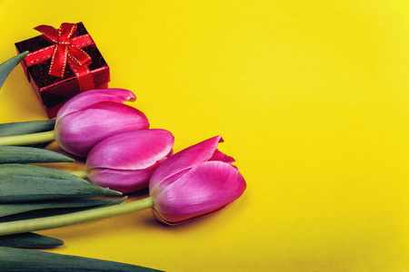 春天的背景，一束美丽的郁金香和黄色背景上的礼品盒