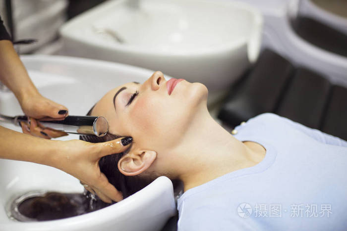 华丽开朗的年轻女人享受头部按摩同时让她的头发被专业的理发师洗美容