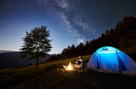 年轻夫妇在营地旁边的篝火旁休息，蓝色的旅游帐篷