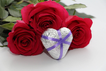 金属心脏被玫瑰包围。 银色的心用丝带装饰。 白色背景上的心和玫瑰。