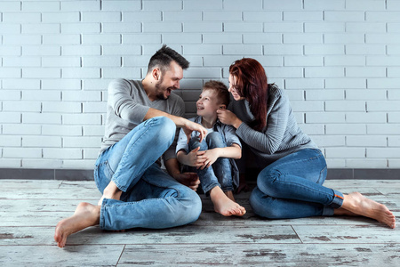 幸福的家庭坐在地板上靠在灰色的墙上。 微笑的夫妇坐在家里。 复制空间。 家庭的概念，他们的住房信贷抵押。