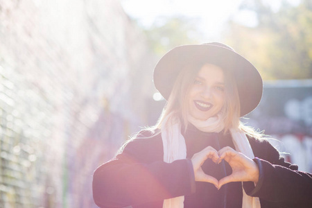 生活方式拍摄可爱的金发女人戴着帽子，在街上展示心脏符号。空的空间
