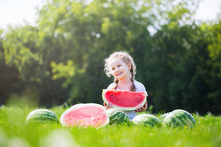 孩子在花园里吃西瓜。 小女孩拿着一片西瓜微笑着。