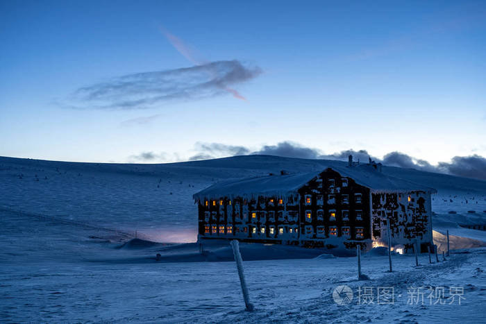 山屋，窗户里有温暖的光线，在被雪景包围的黄昏中发光。