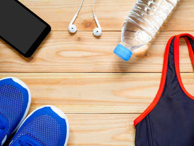 运动和健身设备。 运动胸罩运动鞋手机和瓶装水在健身房的木制背景与复制空间。 上面的风景。 健康概念