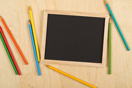 黑色的，空的，空白的黑板，彩色铅笔在棕色的木桌上，从上面平躺着，有复印空间