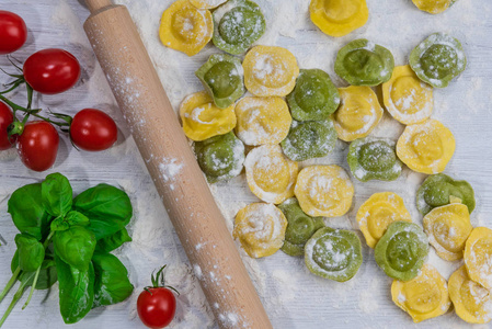 自制新鲜意大利馄饨意大利面在白色木桌上与面粉，罗勒，西红柿，背景，顶部视图。