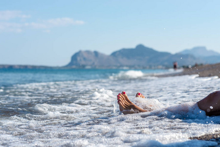 在罗得岛的鹅卵石海滩上，在一片泡沫般的海浪中，用粉红色的踏板特写女性的脚。
