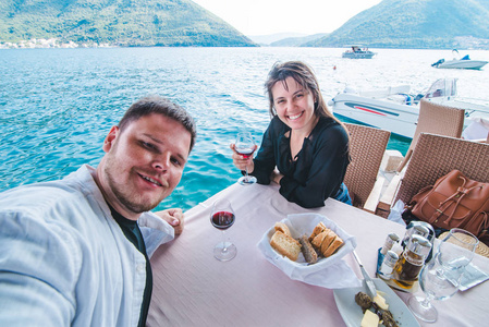 男人和女人在海边的餐馆喝红酒时自拍。背景上美丽的风景