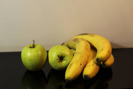两个绿色的苹果在黑色的镜子背景上躺着一根香蕉，上面有反光