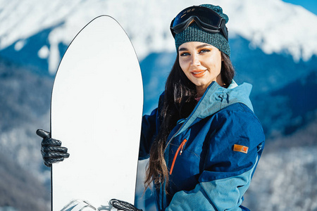 关闭滑雪板女孩微笑和摆姿势在山和坡背景