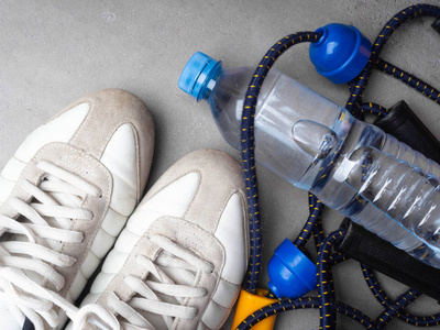 健康的生活方式和运动理念。 灰色背景下的白色运动鞋扩张器和一瓶水