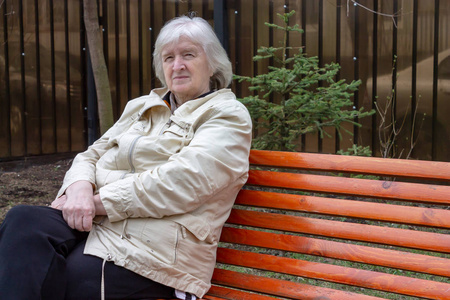 坐在公园长凳上的灰色头发悲伤的老妇人的肖像。