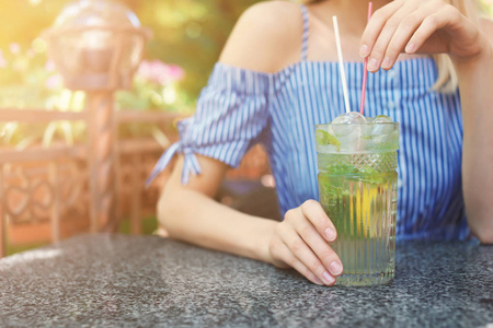 年轻的女人在阳光明媚的一天特写的户外餐桌上喝着一罐清爽的饮料。 文本空间
