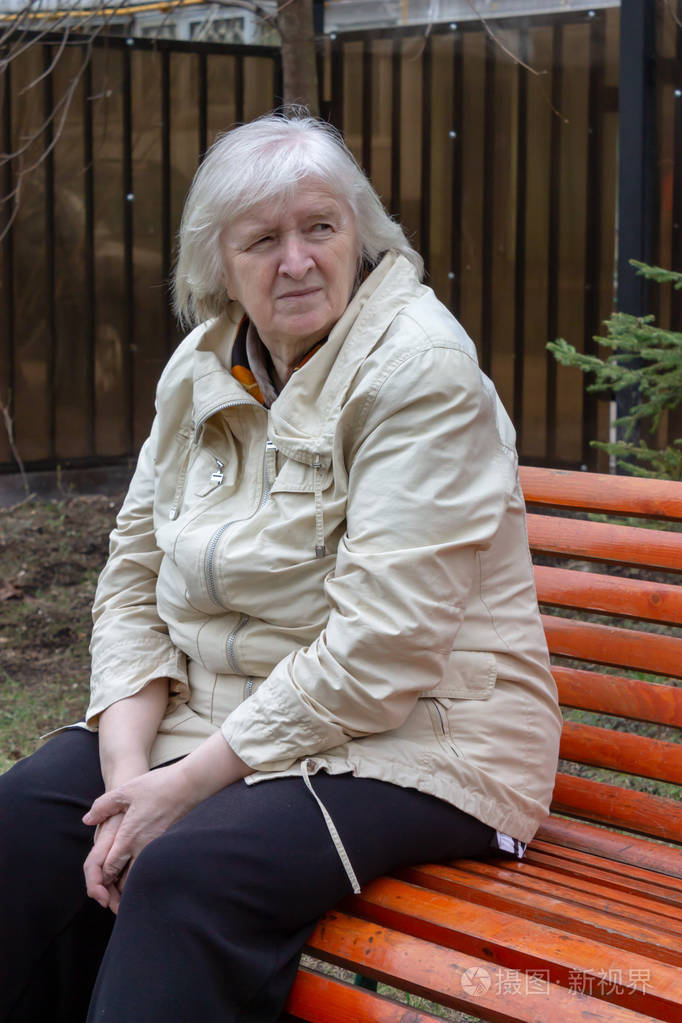 坐在公园长凳上的灰色头发悲伤的老妇人的肖像.
