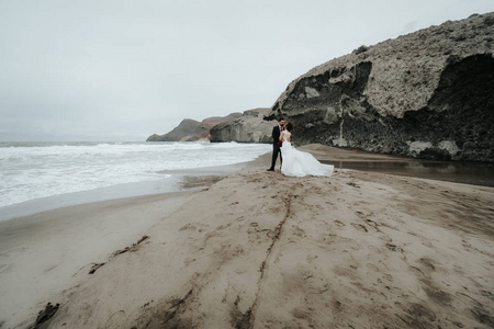 新娘和新郎正沿着海滩散步。 全景。 拥抱。