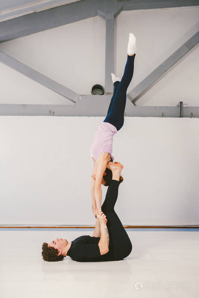 一个年轻的白种男女夫妇在垫子上的白色健身房练习杂技瑜伽.