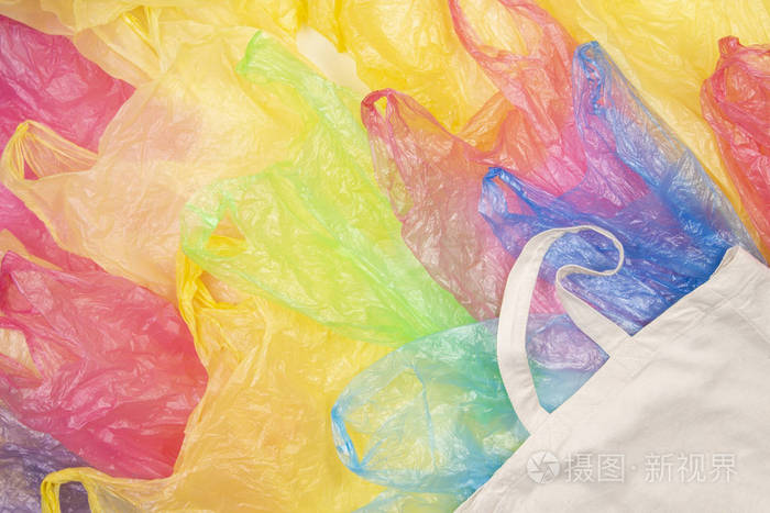 许多五颜六色的塑料袋与一个生态自然可重复使用的购物袋背景.