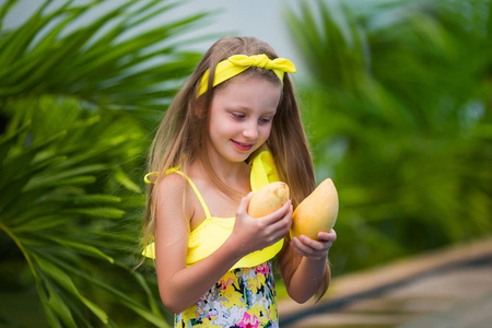 穿黄色泳衣的可爱女孩度假时拿着黄色芒果