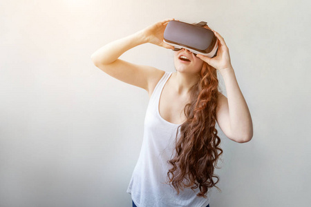 微笑年轻女子戴着虚拟现实VR眼镜头盔耳机在白色背景。 智能手机与虚拟现实护目镜。 科技模拟高科技视频游戏概念