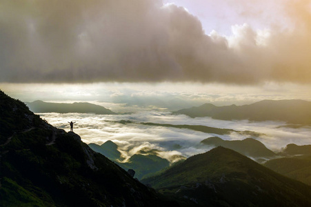 宽山全景。 游客的小轮廓与背包在岩石山坡上，举起手在山谷上覆盖着白色的蓬松云。 自然之美旅游之美和旅游理念