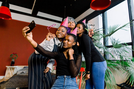 快乐的非洲女孩戴着帽子庆祝生日，并在智能手机上拍照。