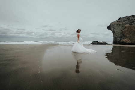 新娘走在海水反射的海滩上。 全景。