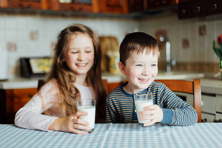 孩子们早上在厨房喝牛奶，玩得开心。 姐姐和哥哥坐在家里的桌子旁