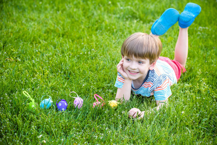 小男孩在复活节的春天花园里寻找复活节彩蛋。 可爱的孩子在草地上躺着鸡蛋排队。 传统兔子庆祝盛宴