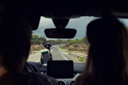 选择性地专注于道路。 近距离拍摄了两个乘坐汽车旅行的女性剪影。 有曲线和标志的长路视野良好。 年轻的司机在电话上使用导航。 模拟