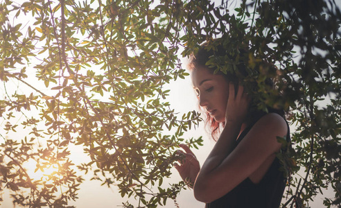 一位美丽的年轻女子的肖像，乌发在树枝和绿叶的框架中，夏天和春天的感官肖像，自然美。