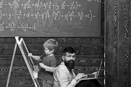 学生在黑板上画画, 老师或父亲在电脑上工作。坐在后面与站立的孩子的侧面看法人