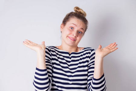 困惑和沮丧的肖像,笨拙的,可爱的,愚蠢的女人耸耸肩,摊开双手,在白色