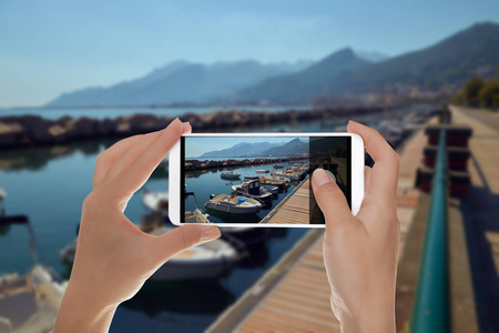 一名男子正在为意大利的一个小码头制作一张照片，照片上的背景是移动电话，上面有山的船只和游艇