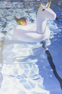 在游泳池里的充气五颜六色的白色独角兽。在带塑料玩具的游泳池度假。在有阳光反射的游泳池里的波纹水。阳光效果。垂直