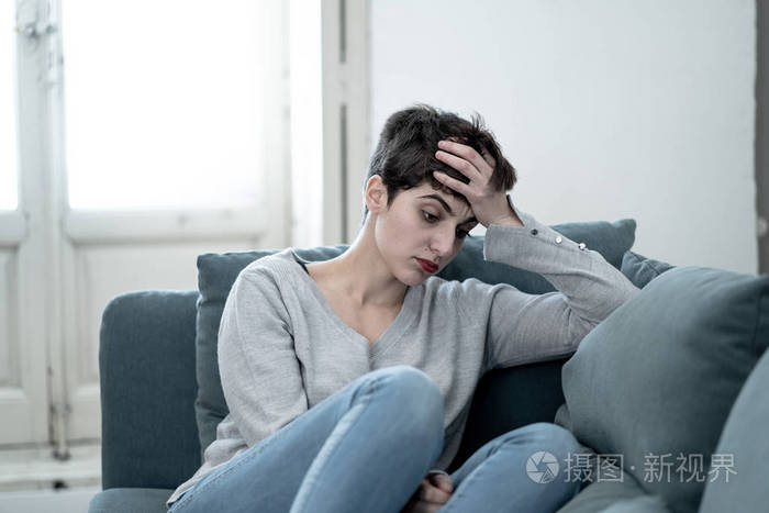 美丽的绝望和沮丧的年轻女人在沙发上感到悲伤,绝望和痛苦的抑郁的人