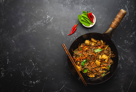 用鸡肉炒荞麦面，蔬菜放在老土炒锅里，筷子放在黑石背景上，特写，俯视..传统亚洲泰餐，文字空间