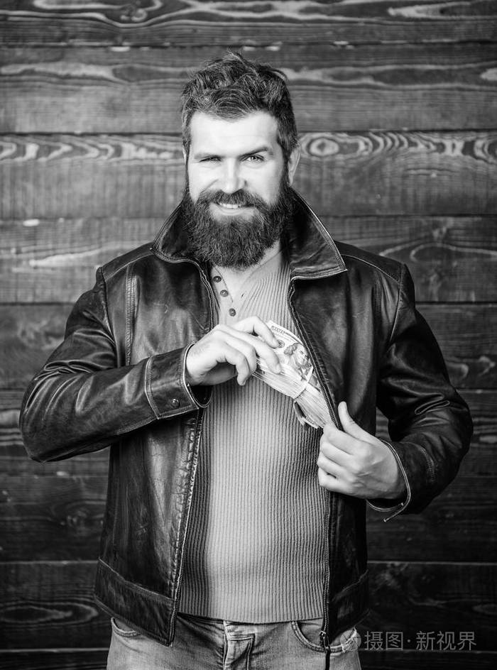 男子残酷的胡须嬉皮士穿着皮夹克, 持有现金.