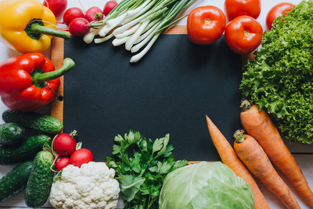 健康的食物概念。 蔬菜沙拉配料边框。 白色木桌上的黑纸空空间背景。 有机海报平面铺设模板。