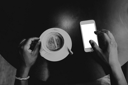 男性手触摸手机的特写镜头视图。非洲男子坐在木桌前使用智能手机。空的空白空白空白屏幕, 供您参考。黑色和白色