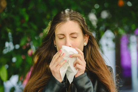 年轻的千禧年病妇打喷嚏，拿着纸巾手帕，吹着擦鼻涕。