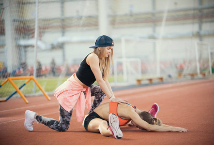 年轻的金发美女在训练结束后帮助另一个女人在体育馆舒展双腿