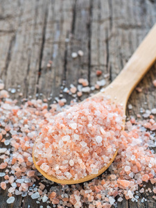 粉红色喜马拉雅盐在勺子上的木制背景。 健康香料特写