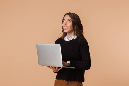 20多岁的美女站着，手提笔记本电脑，与米色背景隔绝
